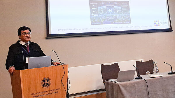 Dr. Mohsen Kazemian steht neben seinem wissenschaftlichen Poster zur Kanalvorhersage in hochmobilen 6G-Netzwerken auf der IEEE-Konferenz CSNDSP 2026.