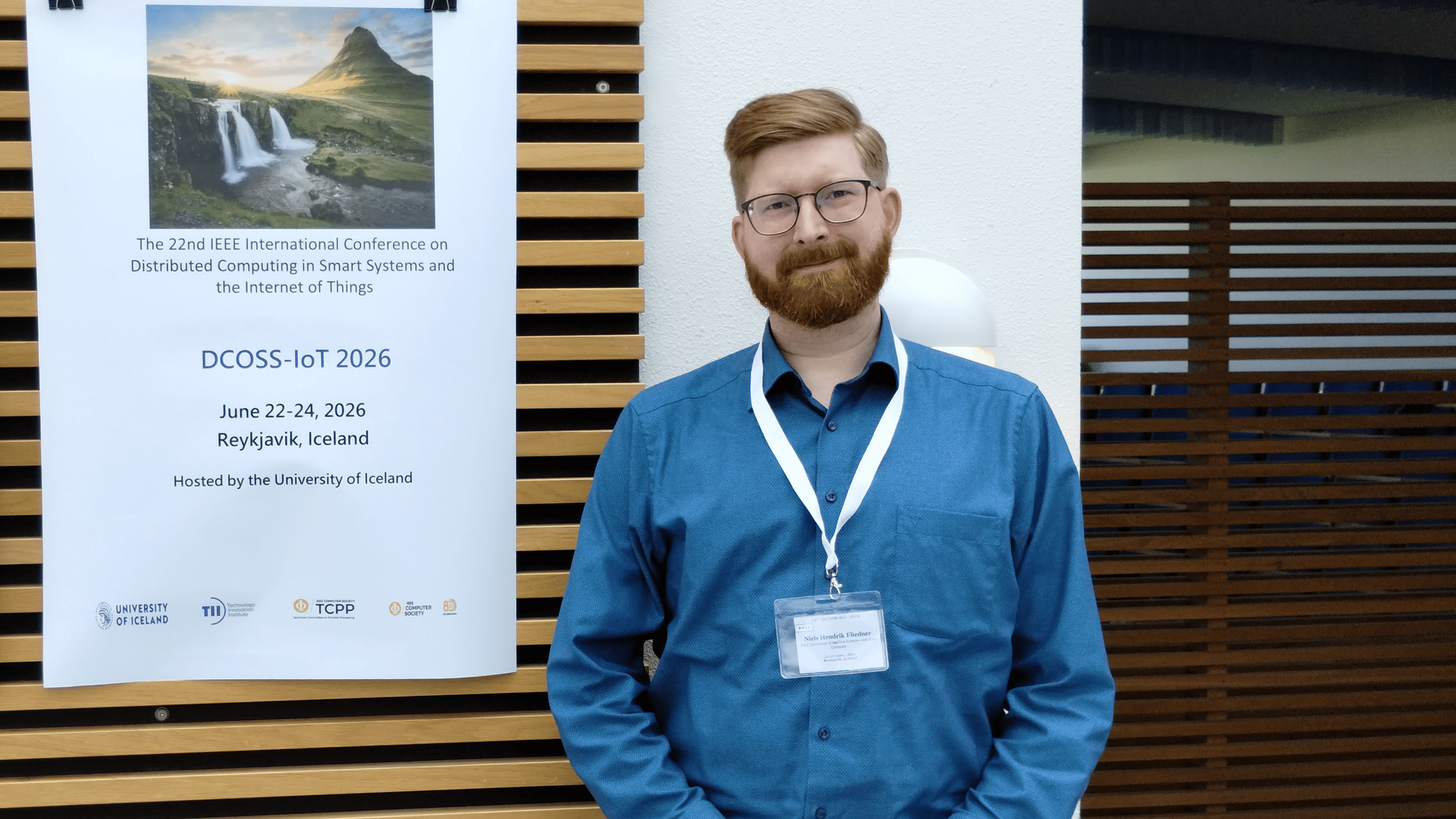 Niels Hendrik Fliedner steht auf der DCOSS-IoT 2026 vor einem Poster