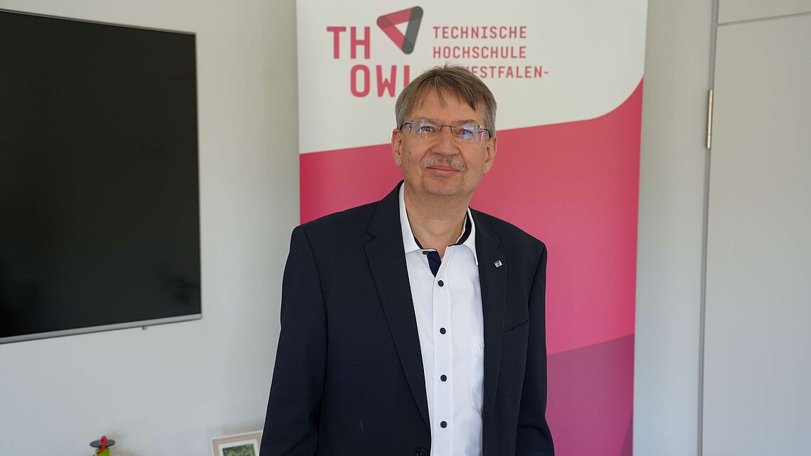 Sen-Prof. Dr. Volker Lohweg steht vor dem Logo der Technischen Hochschule Ostwestfalen-Lippe.