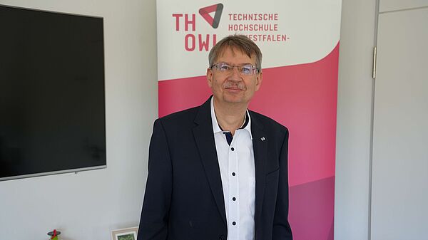 Sen-Prof. Dr. Volker Lohweg steht vor dem Logo der Technischen Hochschule Ostwestfalen-Lippe.