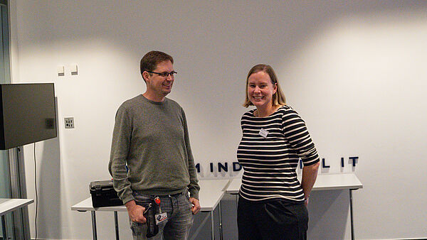 Prof. Dr. Markus Lange-Hegermann und Dr. Sonja Girod stehen nebeneinander im Veranstaltungsraum und lächeln in Richtung Kamera.