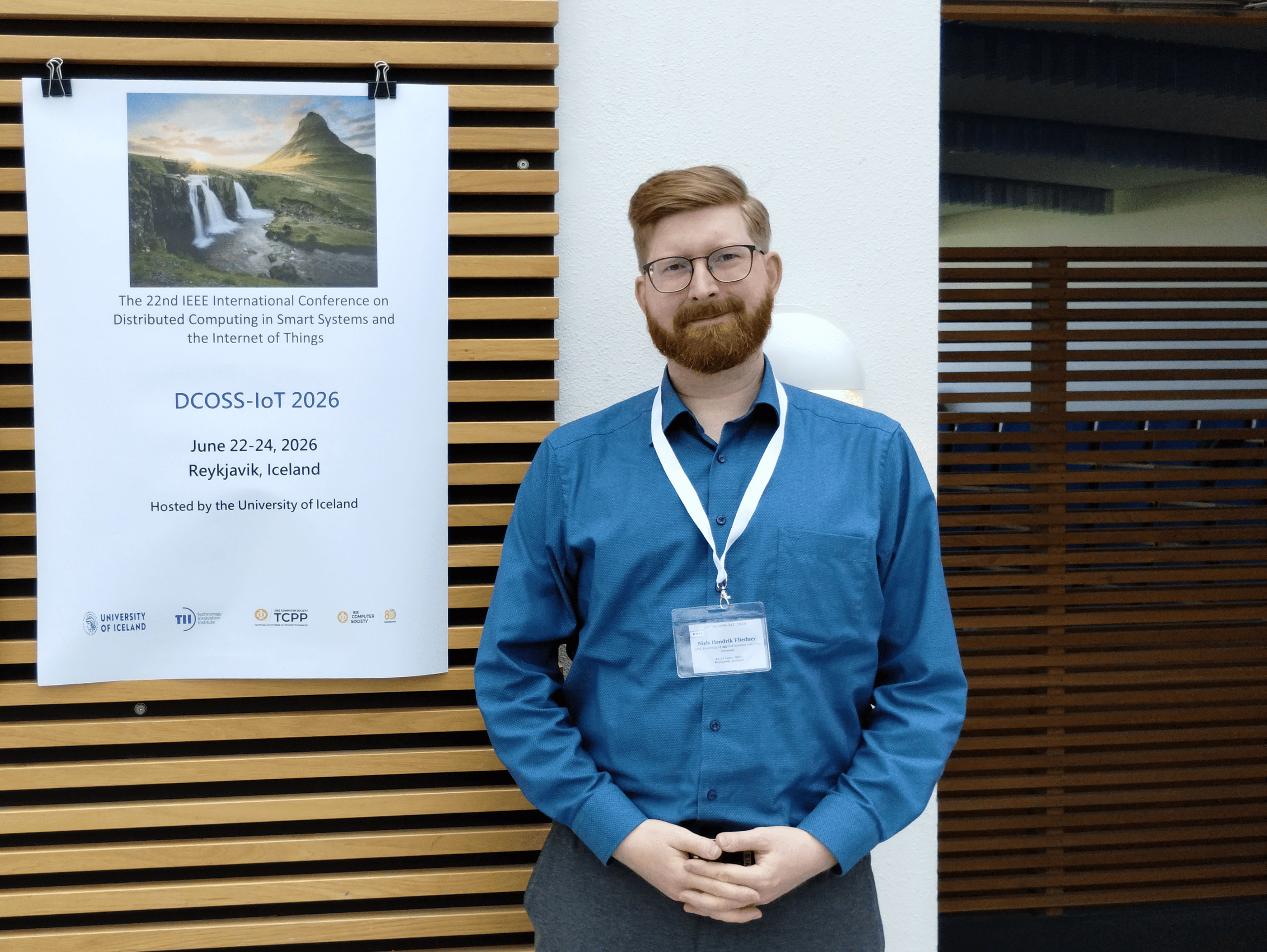 Niels Hendrik Fliedner steht auf der DCOSS-IoT 2026 vor einem Poster